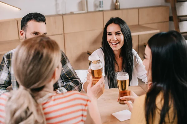 Back view of young women clinking glasses of light beer with friends in pub — Stock Photo