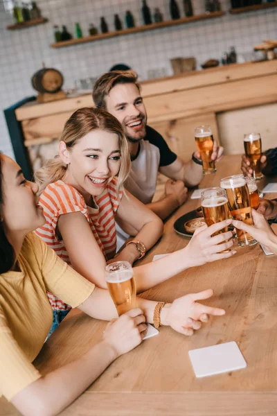 Amigos multiculturais felizes conversando e gesticulando enquanto bebem cerveja no pub juntos — Fotografia de Stock