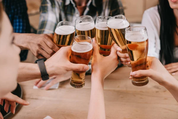 Vista recortada de amigos multiculturales tintineo vasos de cerveza ligera - foto de stock