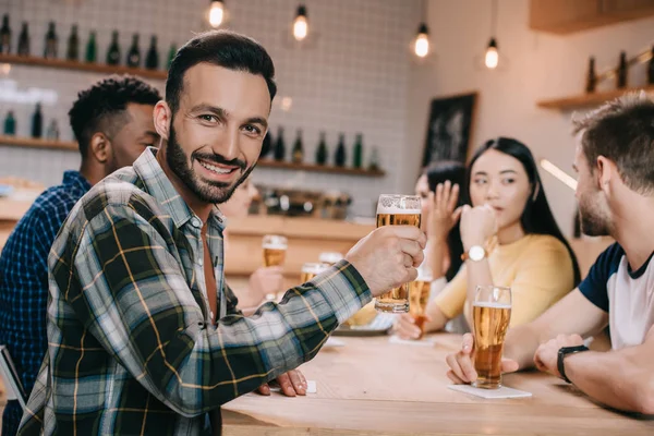 Messa a fuoco selettiva dell'uomo sorridente che guarda la fotocamera mentre tiene in mano un bicchiere di birra — Foto stock