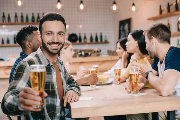 Messa a fuoco selettiva di bell'uomo che sorride alla macchina fotografica mentre tiene in mano un bicchiere di birra — Foto stock