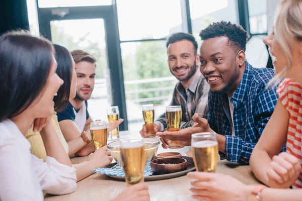 Alegres amigos multiculturales hablando mientras están sentados juntos en el pub - foto de stock