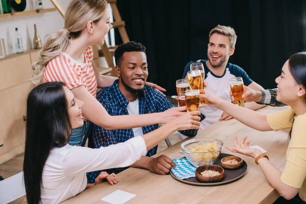 Cheerful multicultural friends clinking glasses of light beer in pub — Stock Photo