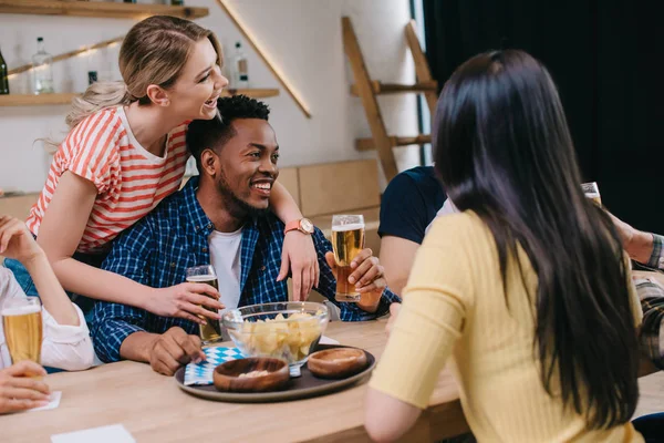 Jeune femme étreignant l'homme afro-américain près d'amis multiculturels dans un pub — Photo de stock