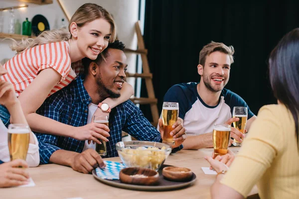 Mulher alegre abraçando homem afro-americano perto de amigos multiculturais no pub — Fotografia de Stock