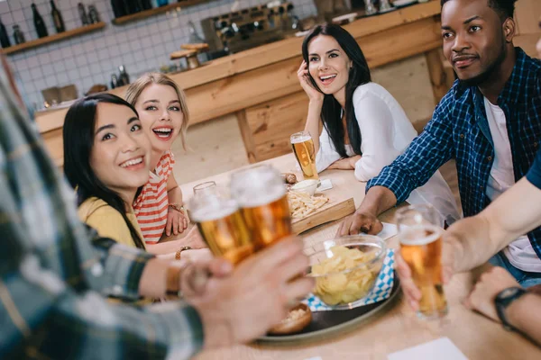 Partial view of man holding glasses of light beer near multicultural friends in pub — Stock Photo