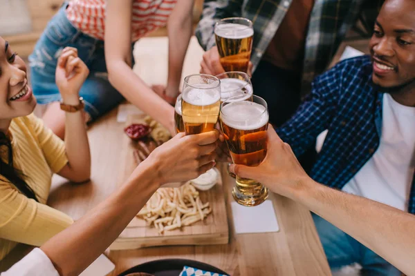 Cropped view of multicultural friends clinking glasses of light beer in pub — Stock Photo