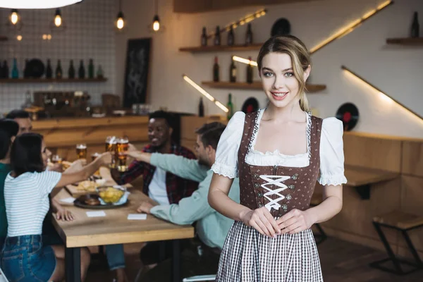 Hermosa camarera en traje nacional alemán sonriendo mientras mira a la cámara - foto de stock