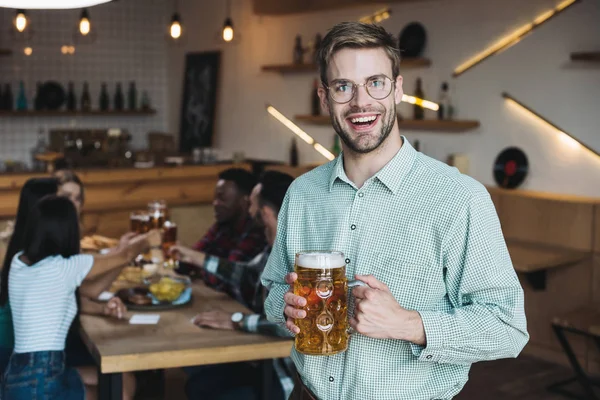 Joven guapo sosteniendo taza de cerveza ligera y sonriendo a la cámara - foto de stock