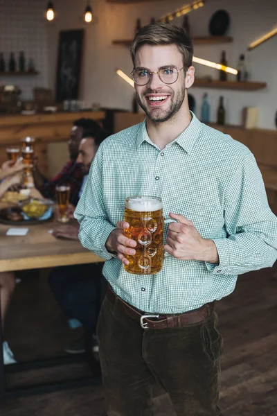 Красивий молодий чоловік тримає кухоль легкого пива і посміхається на камеру — стокове фото