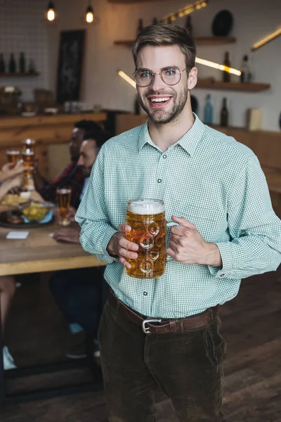 Jovem bonito segurando caneca de cerveja leve e sorrindo para a câmera — Fotografia de Stock