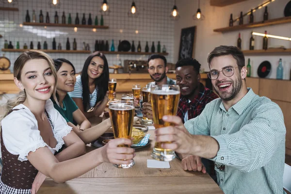 Alegres amigos multiculturales sosteniendo vasos de cerveza ligera y sonriendo a la cámara - foto de stock