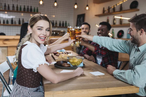 Happy multicultural friends clinking glasses of light beer while celebrating octoberfest in pub — Stock Photo