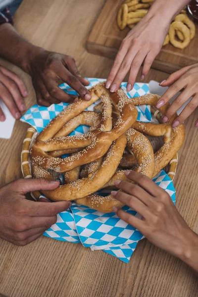 Vue recadrée d'amis multiculturels prenant de délicieux bretzels — Photo de stock