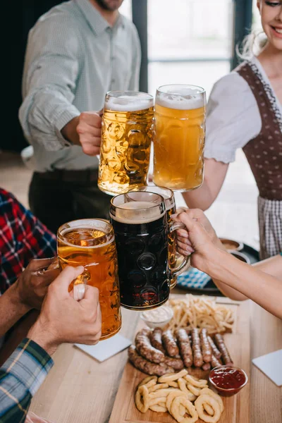 Cropped view of friends clinking mugs of light and dark beer while celebrating octoberfest in pub — Stock Photo