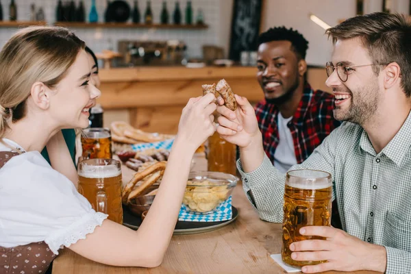 Young woman and woman holding fried sausage while celebrating octoberfest with friends — Stock Photo