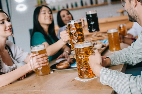 Молодые мультикультурные друзья пьют светлое и темное пиво во время празднования Октоберфеста в пабе — стоковое фото