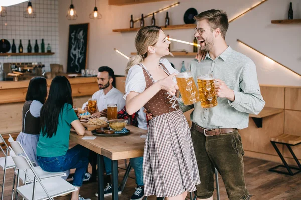 Cheerful man and woman in traditional german costumes holding mugs of beer — Stock Photo
