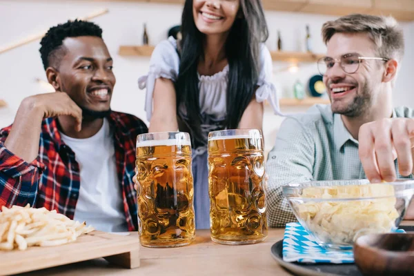 Cropped view of waitress in traditional german costume serving beer for multicultural friends in pub — Stock Photo