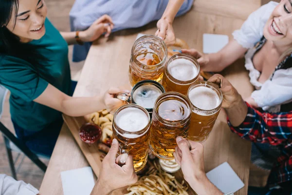 Partial view of multicultural friends clinking mugs of light and dark beer — Stock Photo