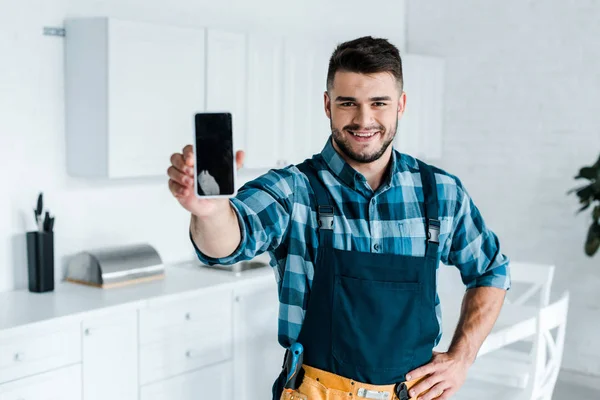 Foco seletivo de feliz handyman barbudo segurando smartphone com tela em branco — Fotografia de Stock