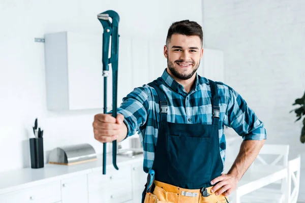 Selective focus cheerful handyman in uniform standing with hand on hip and holding wire cutters — Stock Photo