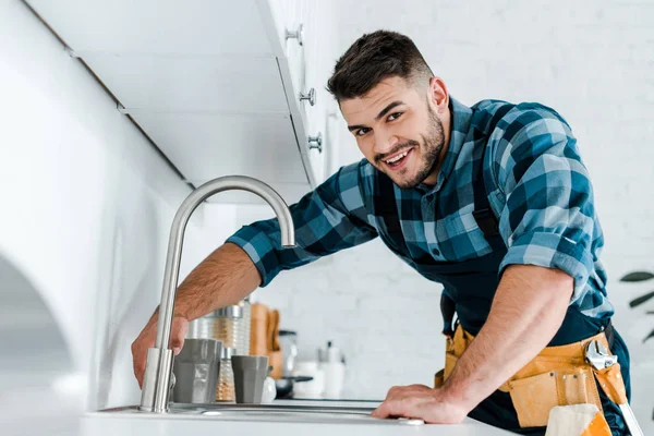 Selective focus of happy handyman working near sink in kitchen — Stock Photo