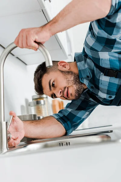 Selective focus of bearded handyman working near sink in kitchen — Stock Photo