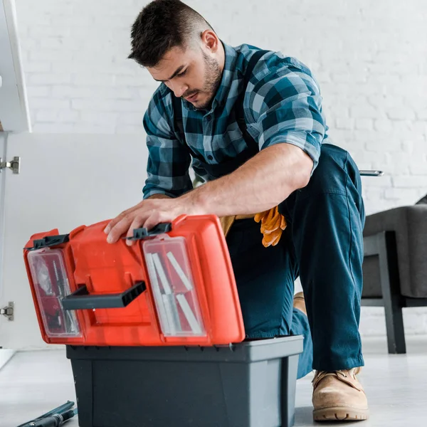 Schöner Handwerker schaut auf geöffnete Werkzeugkiste in Küche — Stockfoto