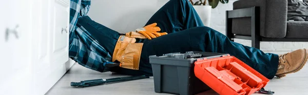 Tiro panorâmico de faz-tudo que trabalha na cozinha perto da caixa de ferramentas enquanto deitado no chão — Fotografia de Stock