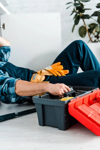 Vista recortada del reparador que trabaja en la cocina cerca de la caja de herramientas mientras está acostado en el suelo - foto de stock