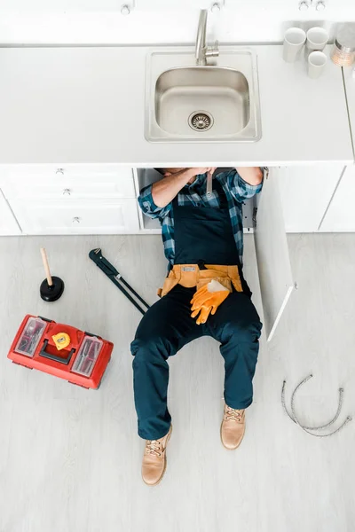 Draufsicht auf Handwerker, der auf dem Boden liegt, während er in der Nähe des Werkzeugkastens arbeitet — Stockfoto