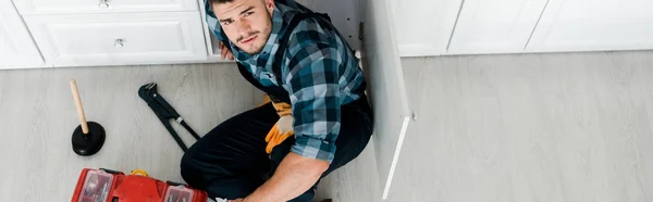 Panoramic shot of bearded handyman sitting on floor near toolbox — Stock Photo