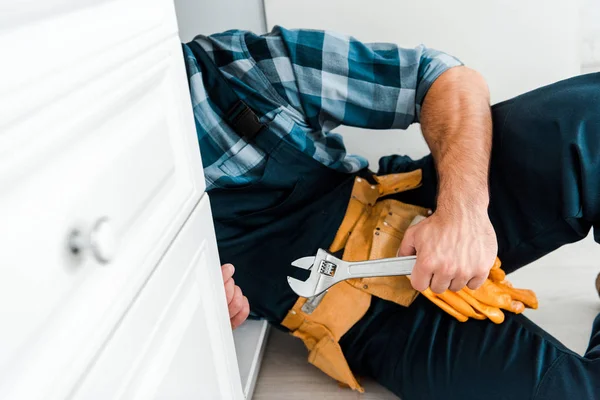 Vista cortada de handyman segurando chave ajustável perto do armário da cozinha — Fotografia de Stock