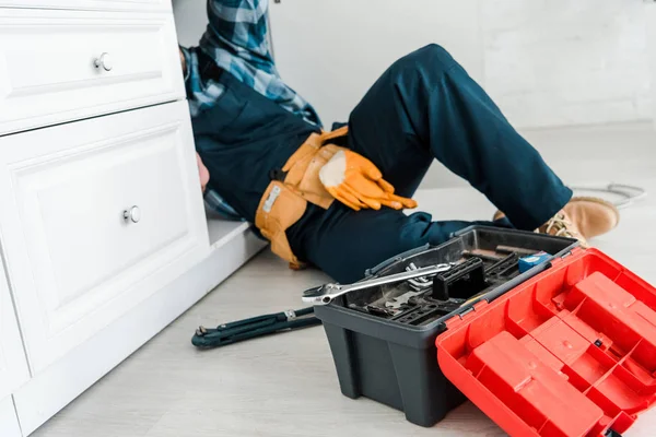 Selective focus of repairman working near kitchen cabinet and toolbox — Stock Photo