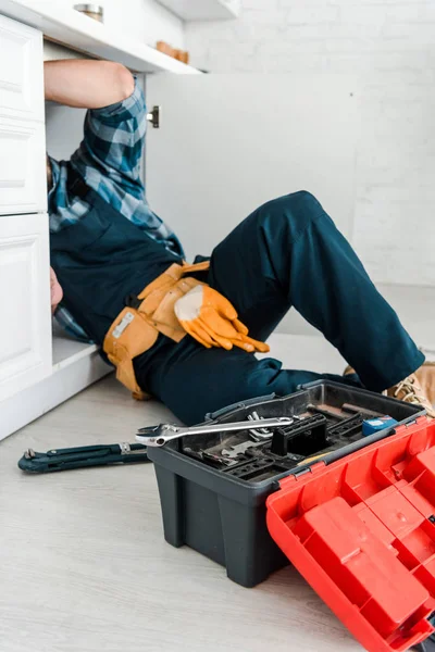 Vista cortada do reparador que trabalha perto do armário da cozinha e da caixa de ferramentas — Fotografia de Stock