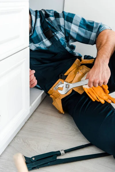 Обрізаний вид ремонтника, що тримає регульований ключ біля кухонного шафи — стокове фото