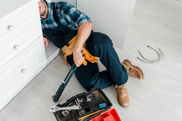 Обрезанный вид бородатого ремонтника, работающего возле кухонного шкафа и ящика с инструментами — стоковое фото