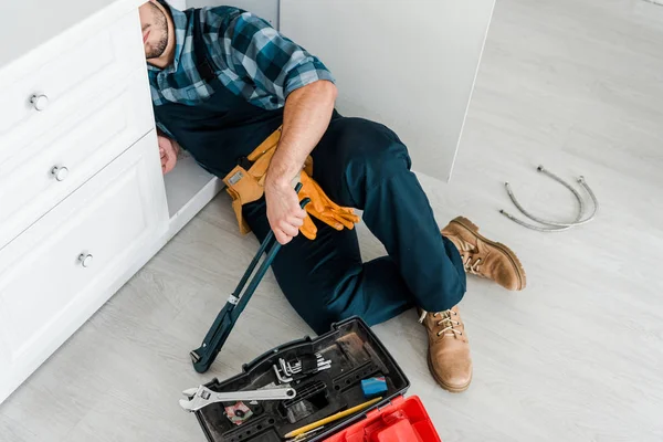 Vue recadrée du réparateur barbu travaillant près de l'armoire de cuisine et de la boîte à outils — Photo de stock