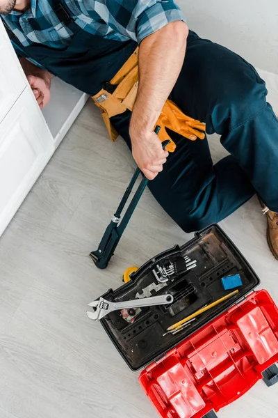 Vista recortada del reparador trabajando cerca del gabinete de la cocina y caja de herramientas con instrumentos - foto de stock