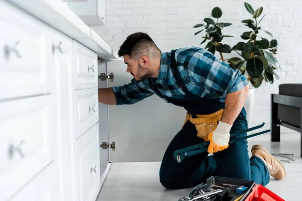 Foco seletivo do homem barbudo que trabalha na cozinha perto da caixa de ferramentas com instrumentos — Fotografia de Stock