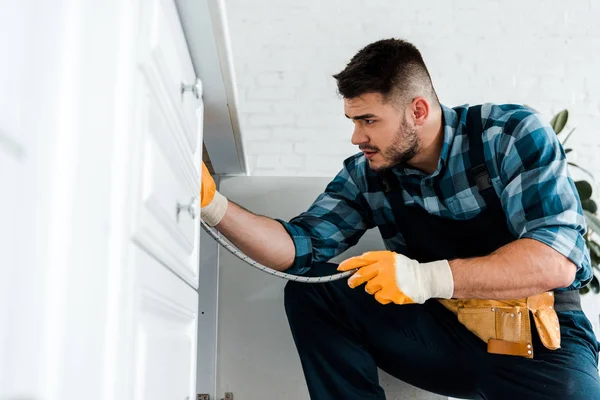 Selective focus of repairman holding metal hose near kitchen cabinet — Stock Photo