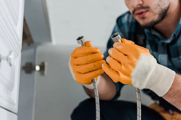 Foco seletivo do faz-tudo segurando mangueira de metal perto do armário da cozinha — Fotografia de Stock