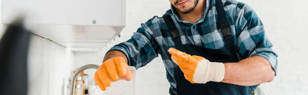 Panoramic shot of handyman in rubber gloves standing in kitchen — Stock Photo