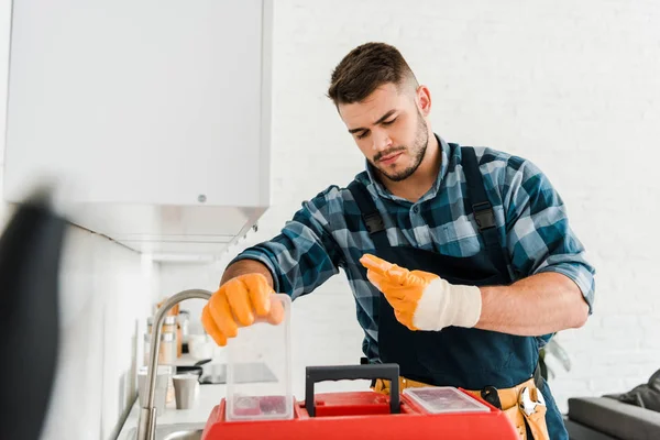 Messa a fuoco selettiva di handyman bello guardando cassetta degli attrezzi in cucina — Foto stock