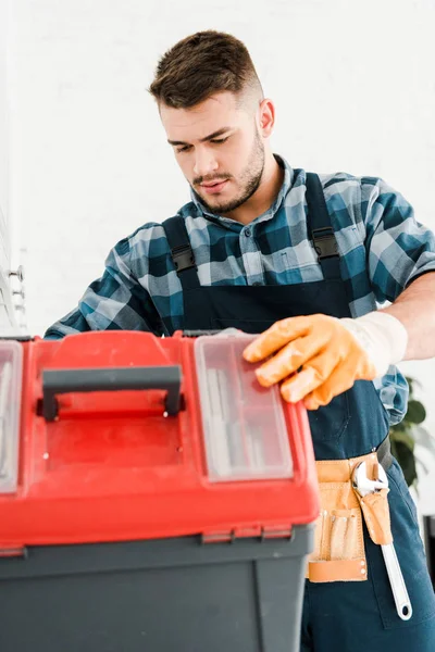 Schöner Handwerker schaut auf Werkzeugkiste in Küche — Stockfoto