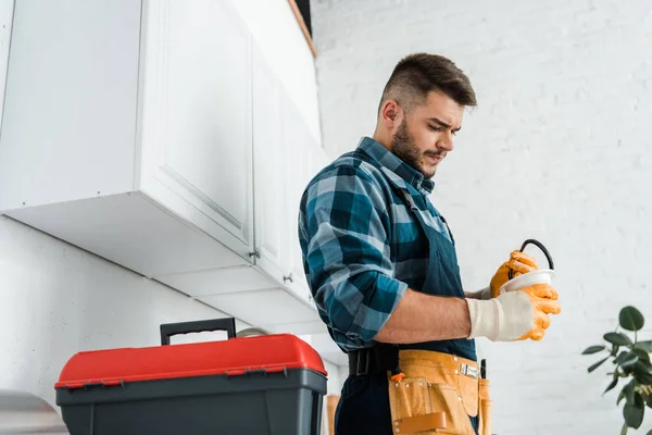 Guapo barbudo hombre sosteniendo embudo cerca de caja de herramientas en cocina - foto de stock