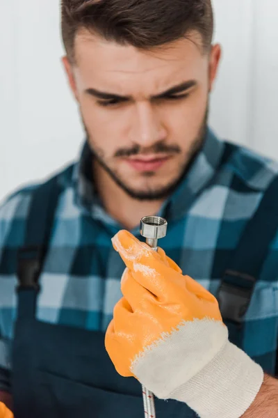 Selective focus of handsome repairman in rubber glove looking at metal hose — Stock Photo