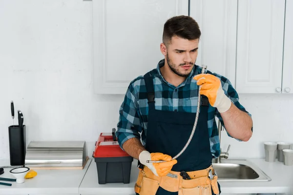 Bearded  repairman in rubber gloves looking at metal hose — Stock Photo