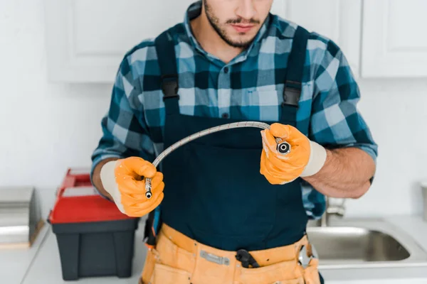 Cropped view of bearded repairman in rubber gloves holding metal hose — Stock Photo